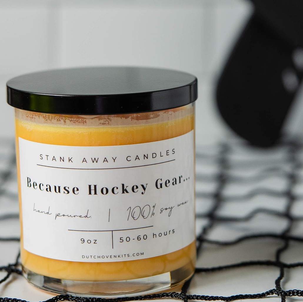 picture of an orange, sweet orange and chili pepper scent candle sitting on a hockey net with hockey sticks in the background. Because Hockey Gear