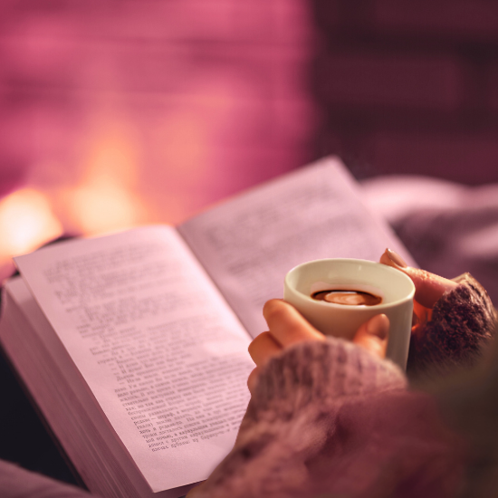 image of someone holding a mug and reading a book by a cozy fireplace