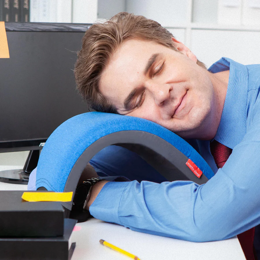 A man sleeping on a nap pillow with an arc design on his work desk.