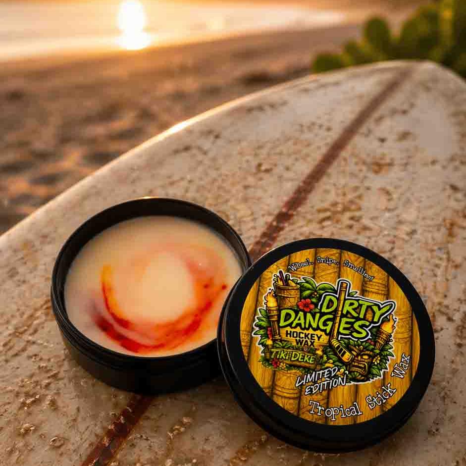 An open tin of dirty dangles tiki deke limited edition tropical stick wax on a rustic surfboard at the beach