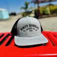 a light gray and black dirty dangles hockey co mesh snapback trucker hat outside on a red lawn mower.