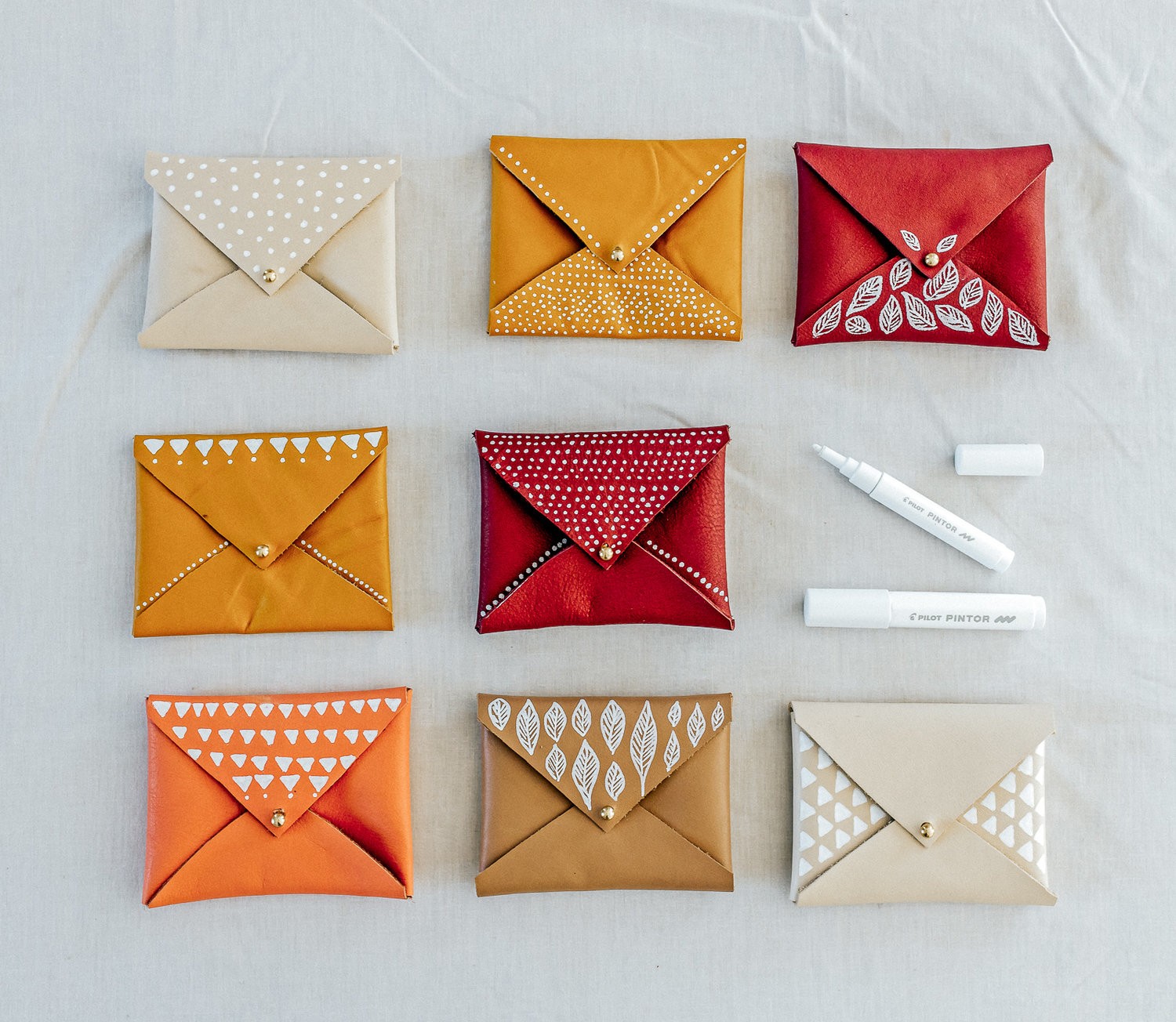 A group of no-sew leather pouches lie on a table with white markers.