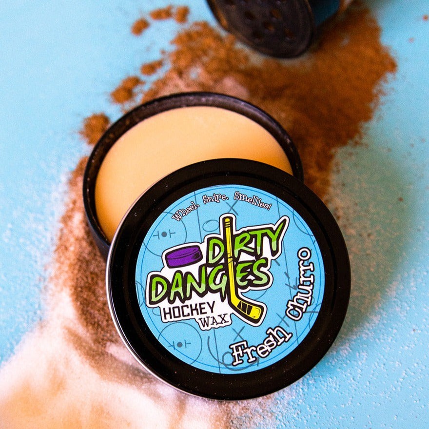 A tin of dirty dangles hockey stick wax fresh churro scent. Tan in color on a blue background with cinnamon and sugar.