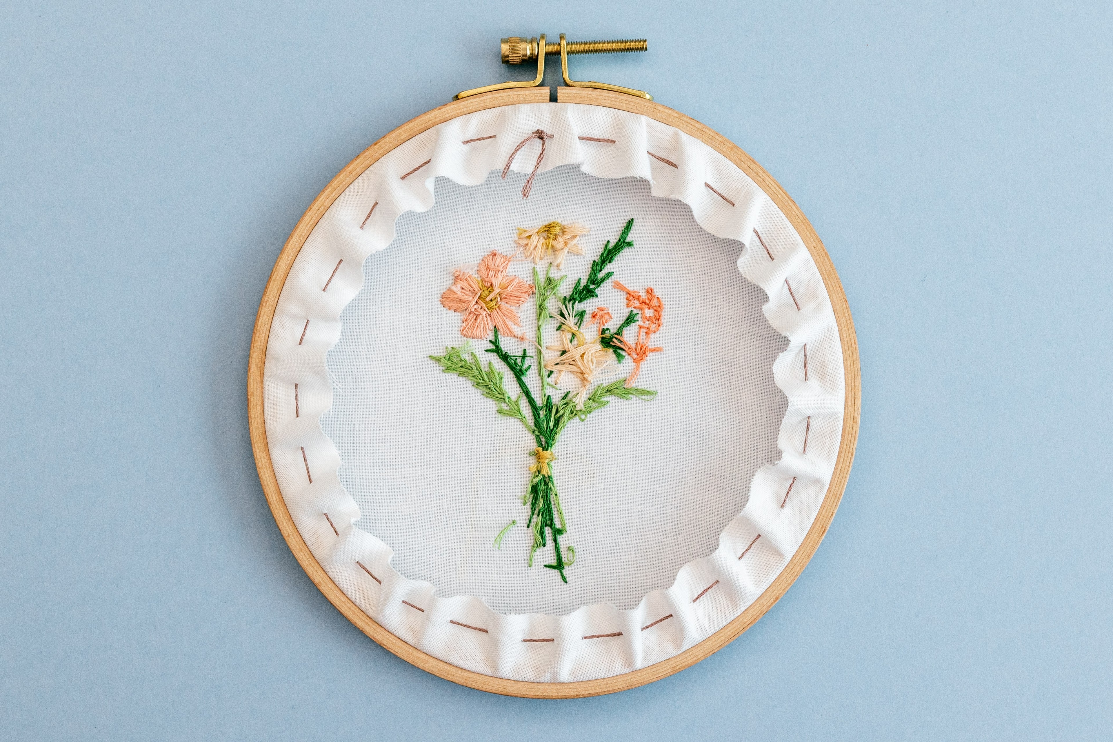 A finished hoop lies on the table, with a running stitch back.