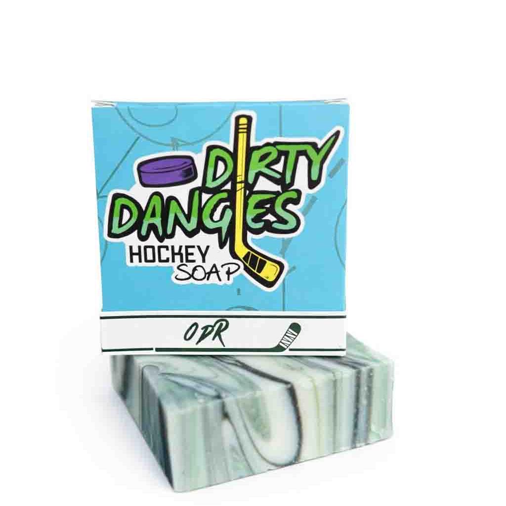 A bar and box of Dirty Dangles ODR soap on the boards of an outdoor ice rink. A green, black and white swirl soap bar,