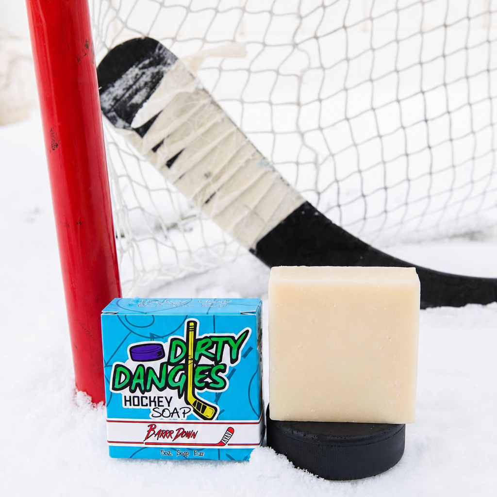 A black soap bar sits in the snow with a hockey goal, hockey puck and a hockey stick. Puck Drop