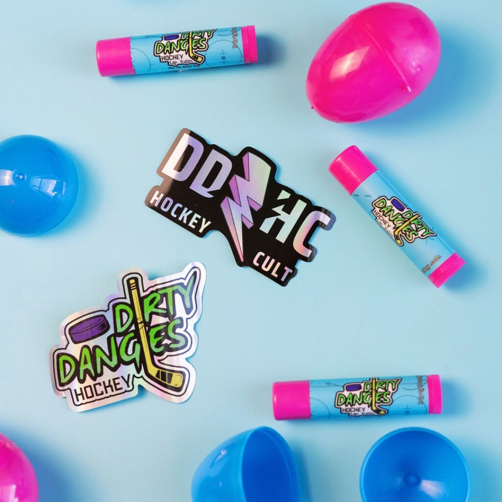 3 tubes of dirty dangles hockey lip balm on a blue background with a ddhc sticker and blue and pink easter eggs