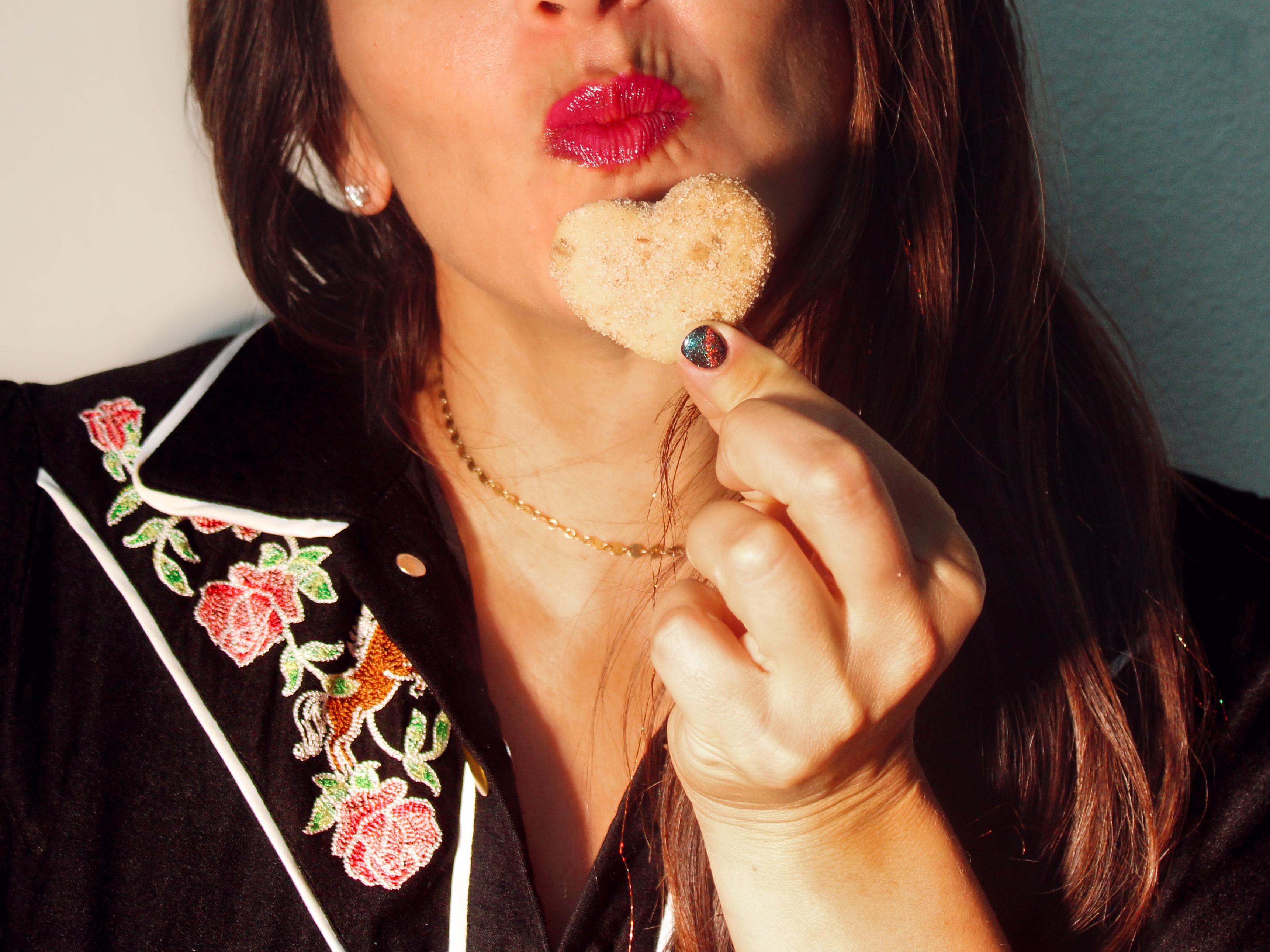 woman in black jumper holding up cookie to lips close up