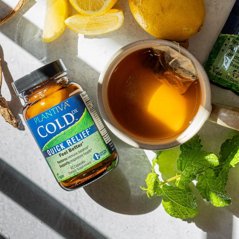 A bottle of ColdDx lying on a white counter next to a cup of tea with lemon and mint