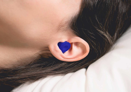 A blue earplug fitted into the ear of head lying down on a pillow.