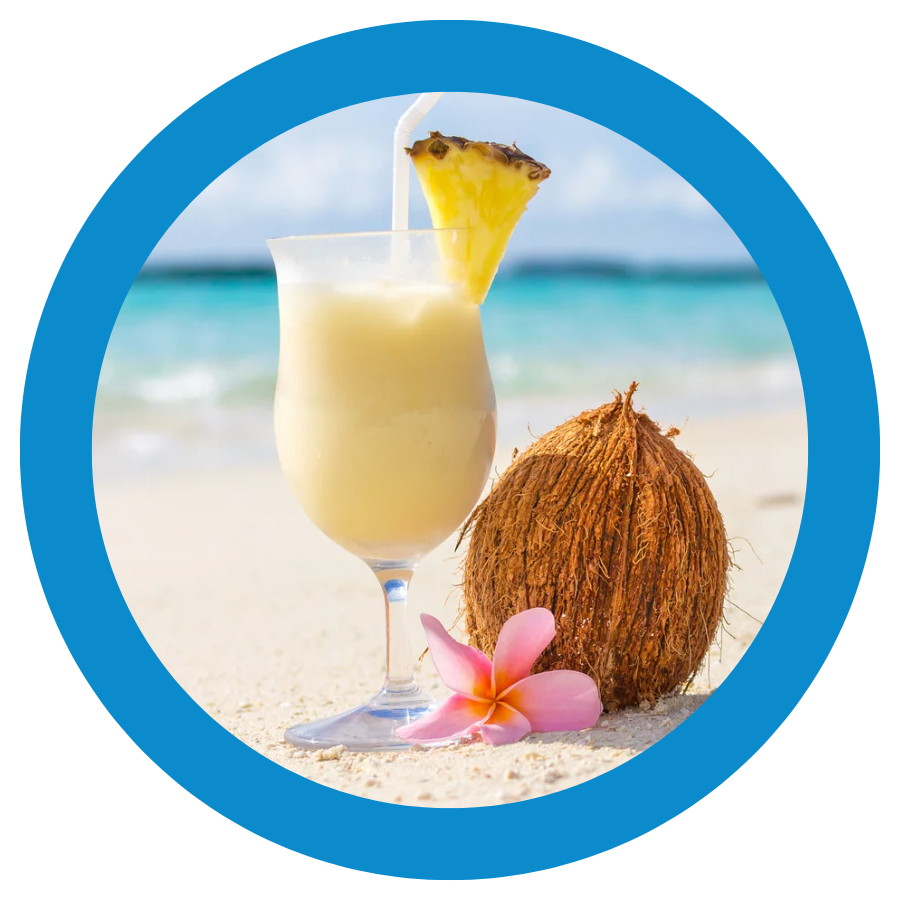 A piña colada and a coconut on a beach.