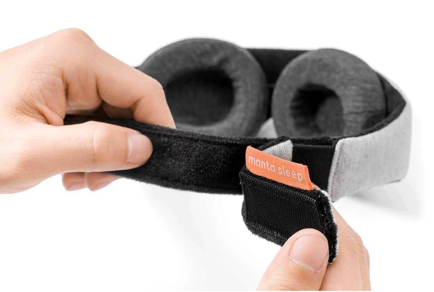 Hands holding the Velcro closure of a sleep mask with eye cups.