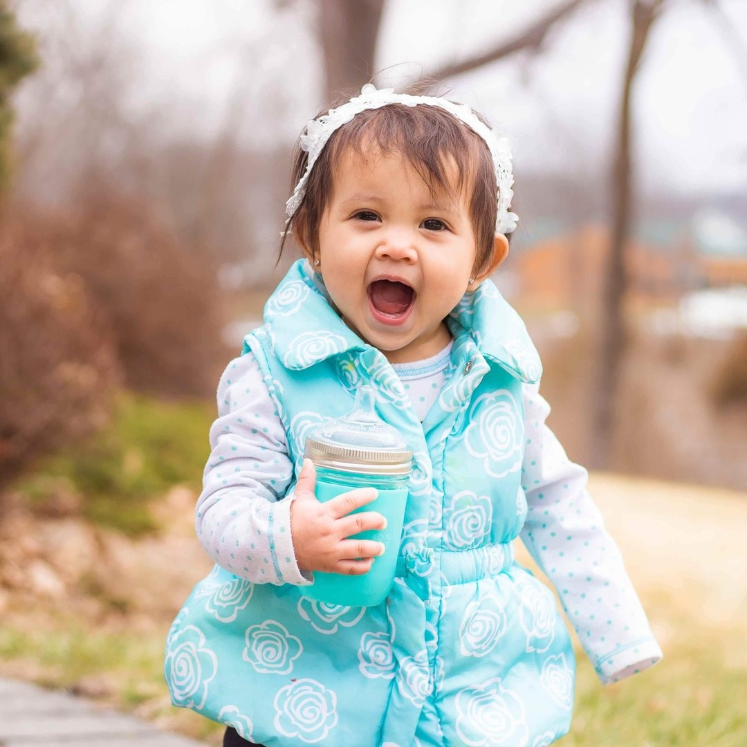 toddler girl smiling outside with glass baby bottle