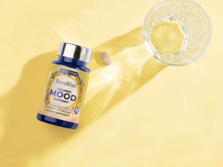 BacoBliss supplement bottle next to it's tablet and a glass of water on a yellow background.