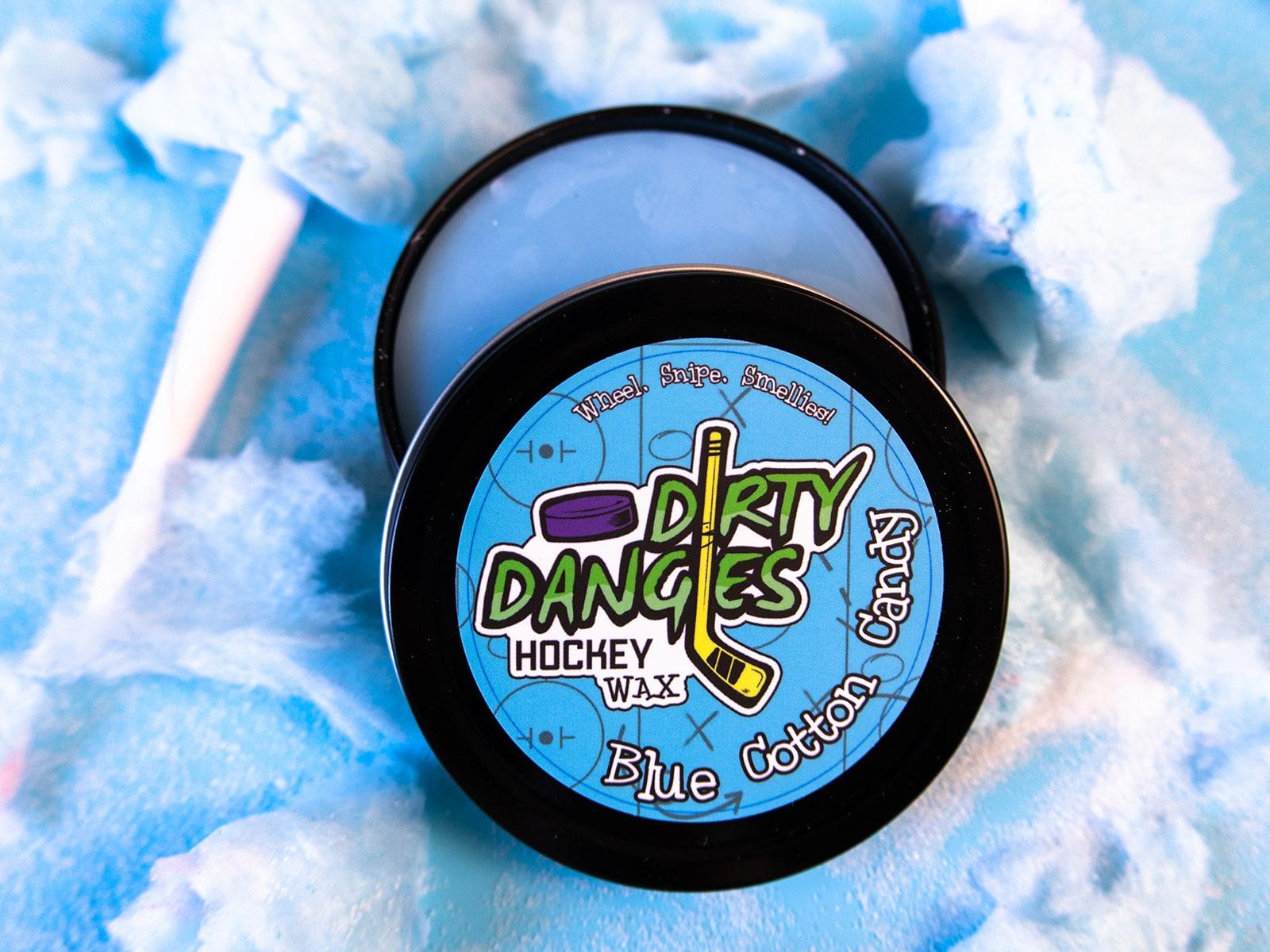 A tin of Dirty Dangles Hockey Stick Wax Blue Cotton Candy Scent sits open on a blue background surrounded by blue cotton candy.