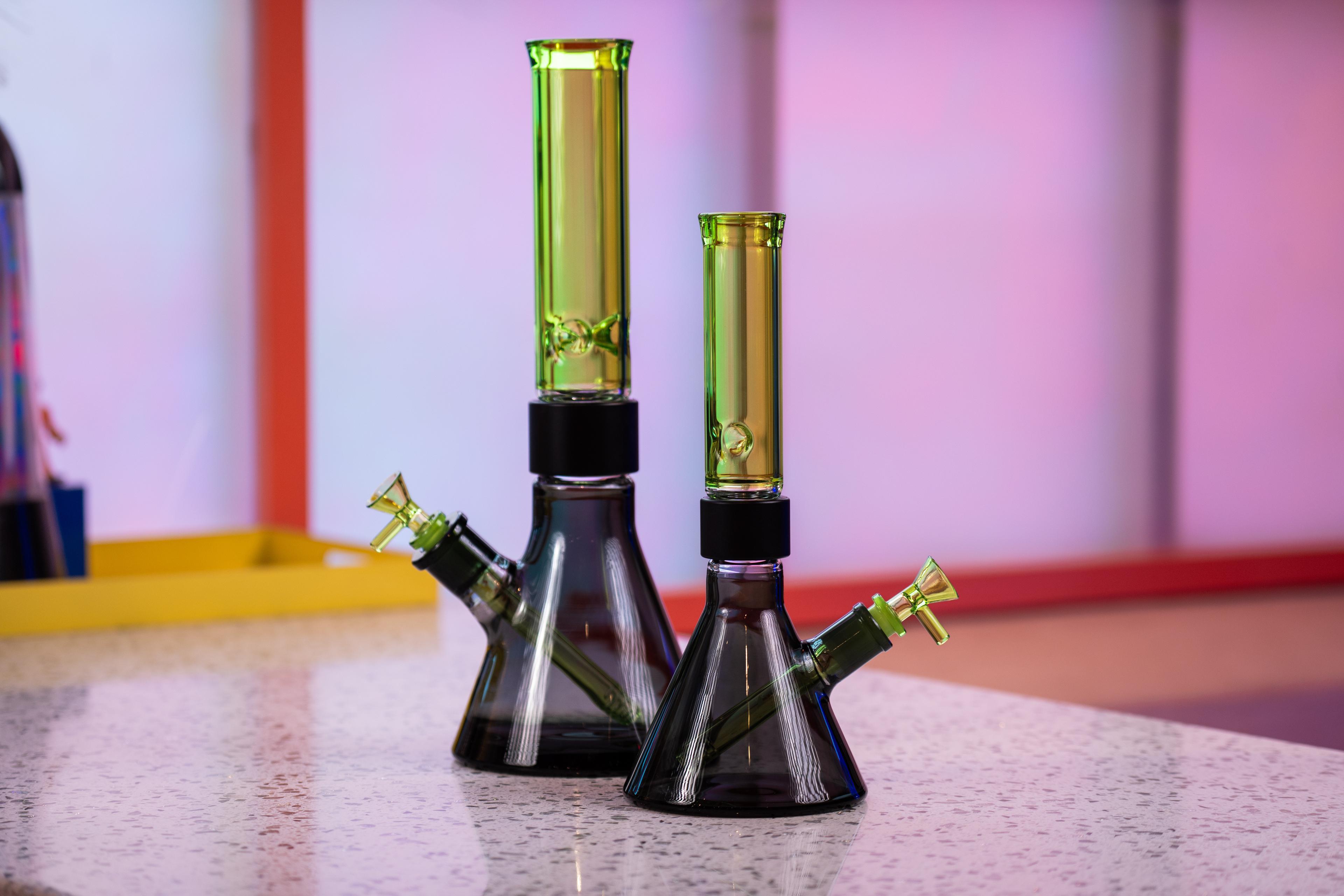 A side-by-side comparison of two green and black Prism modular glass bongs from the Duo Collection. On the left is the MINI size and on the right is the Classic size, both featuring Slime Green glass mouthpieces, black anodized aluminum Halo Connectors, and Midnight Black beaker bases.