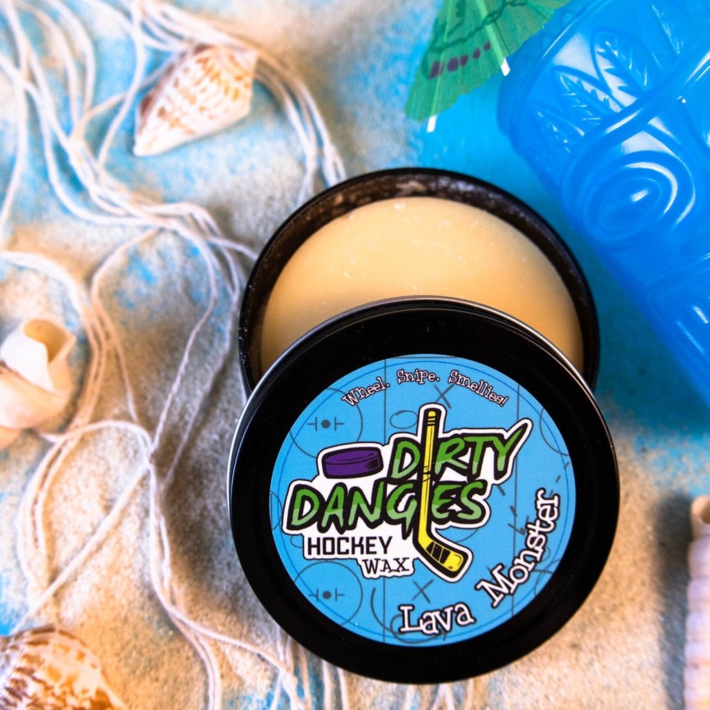 A tin of dirty dangles hockey stick wax lava monster scent. Orange in color on a blue background with seashells and a tiki drink.