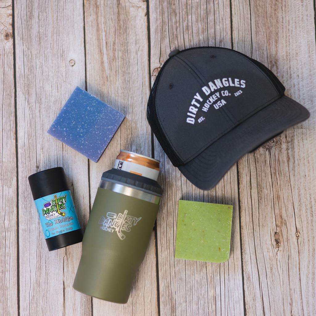 2 bars of hockey soap, a Tactical Green 2 in 1 drink tumbler can holder, a stick of dirty dangles natural deodorant and a dirty dangles hockey co. hat on a wood background.