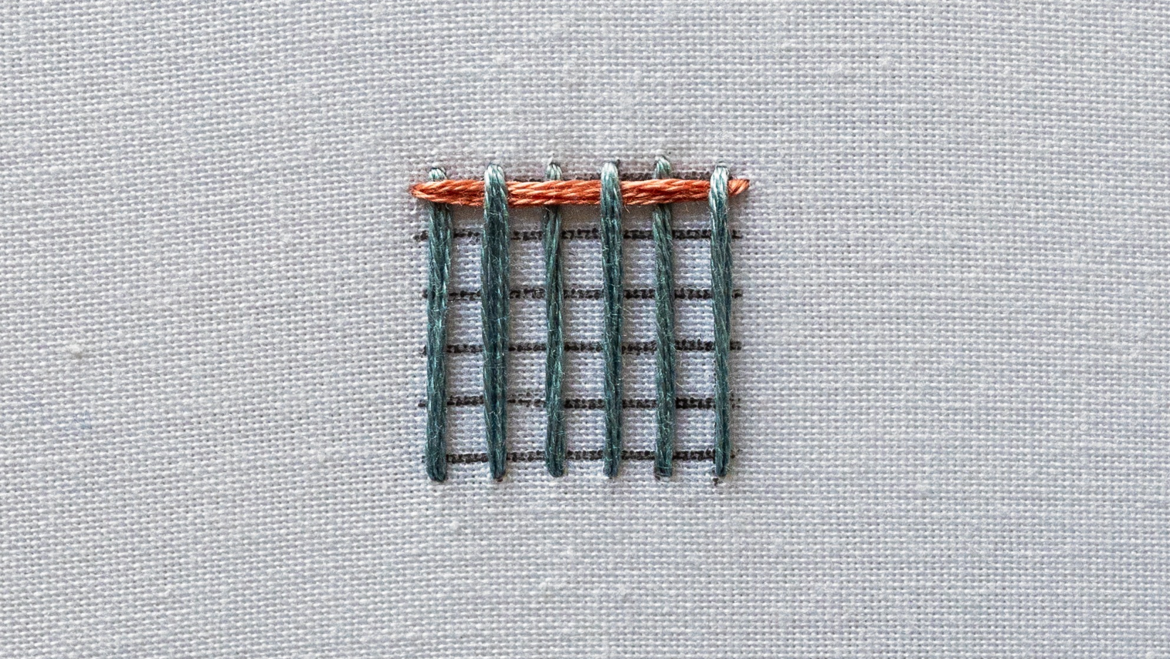A completed first row of weaving passing over and under the warp threads.