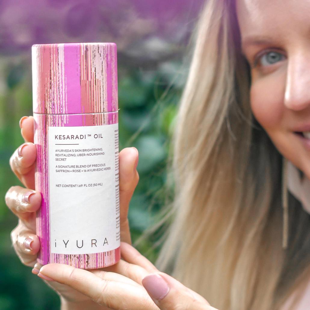 A Kesaradi Oil user holding up their bottle amid beautiful rose vines