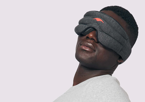 A man leaning backward while wearing a dark gray weighted sleep mask.