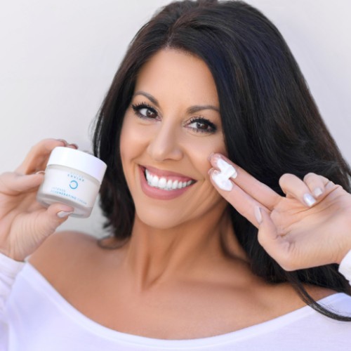mature woman smiling and holding up Noche's Ocean Caviar Face Cream.