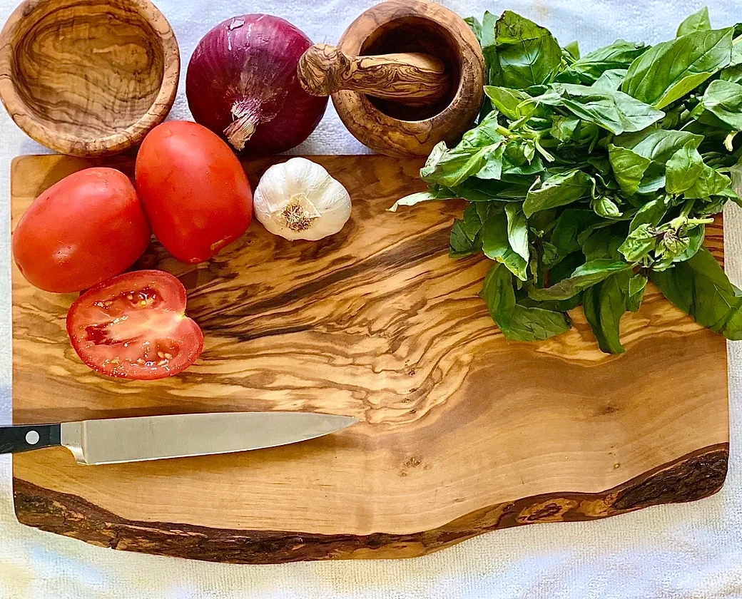 olive wood cutting board with tomato, basil, garlic and a red onion