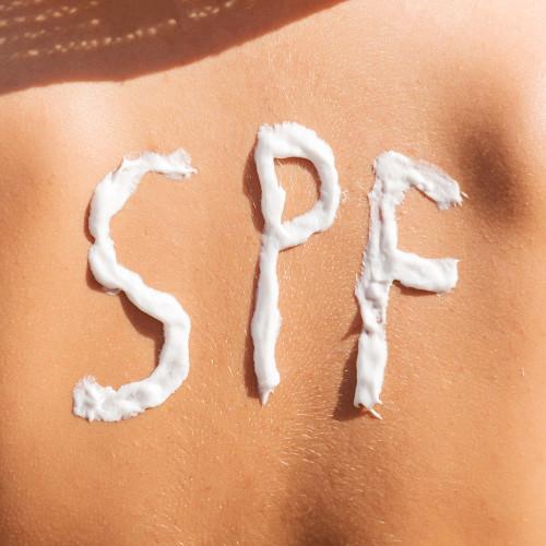 woman's back with the word "SPF" spelled out in sunscreen.