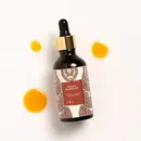 A bottle of manjish glow exilir surrounded by a few drops of serum