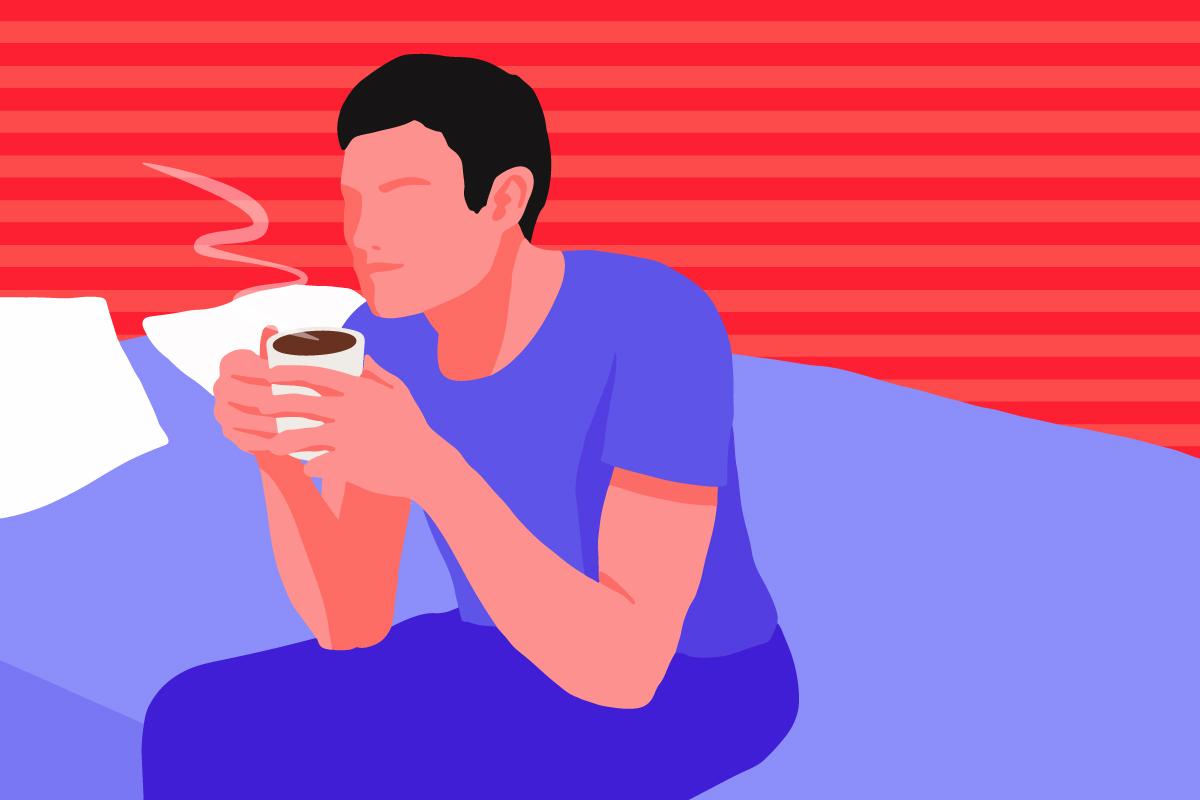 A man holding a cup of hot chocolate, sitting on a bed.