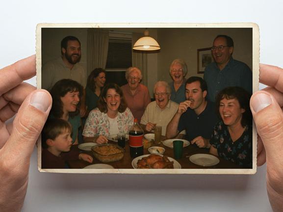 Close-up of hands holding an old photo of a large family smiling and gathered around a dinner table.