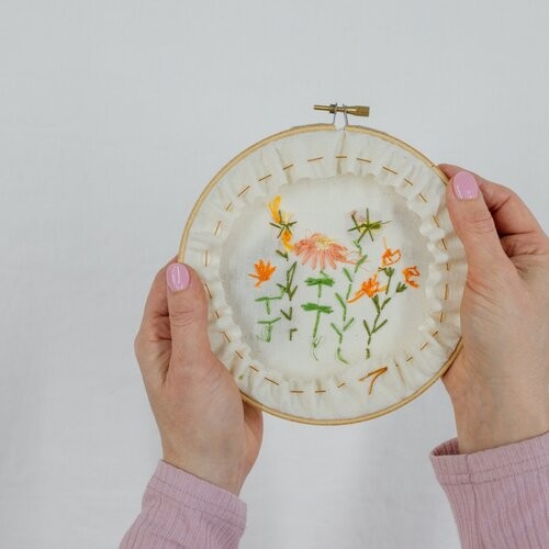 A hand holds up a finished and framed embroidery creation.