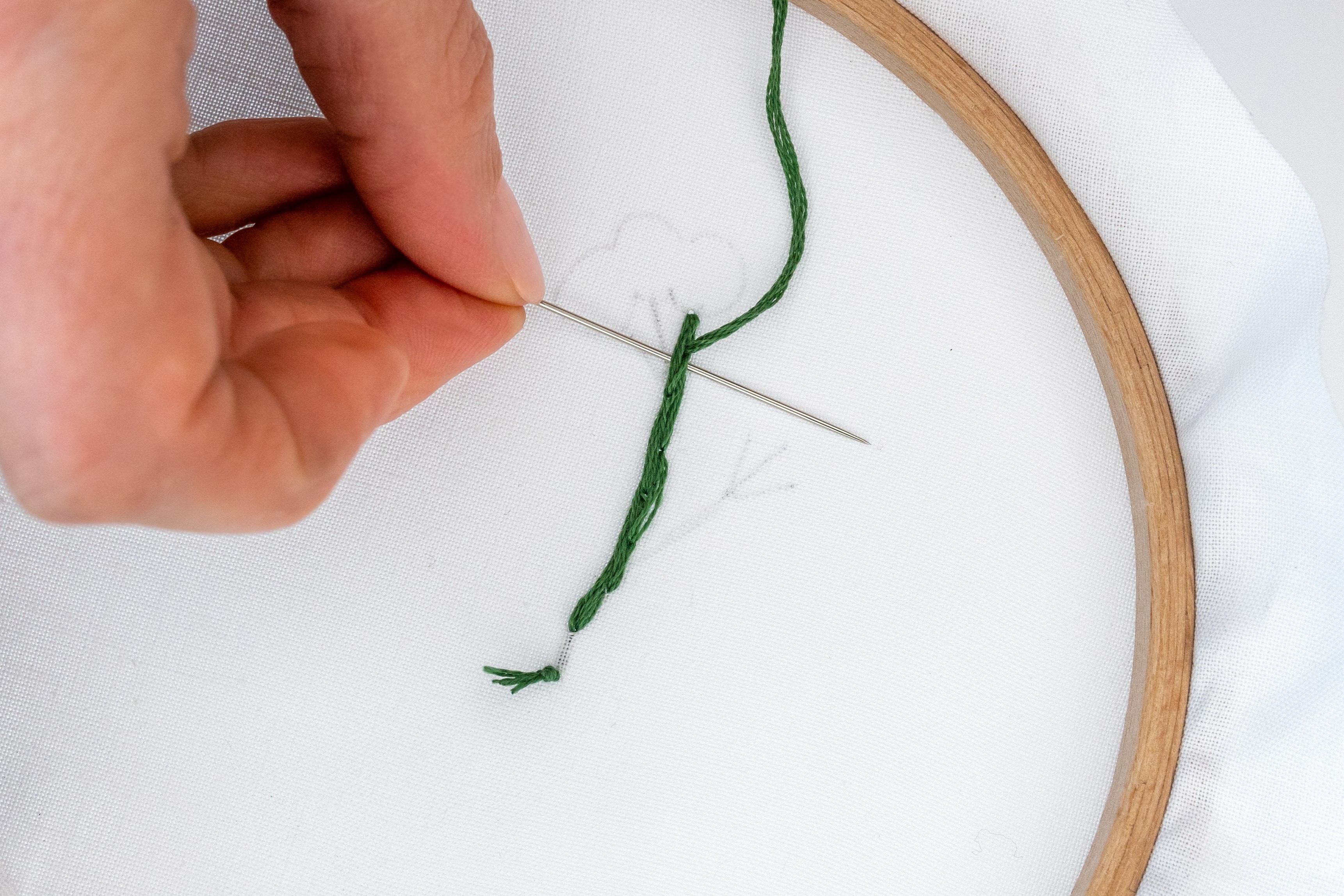 A hand pushes a needle through the back of stitching.