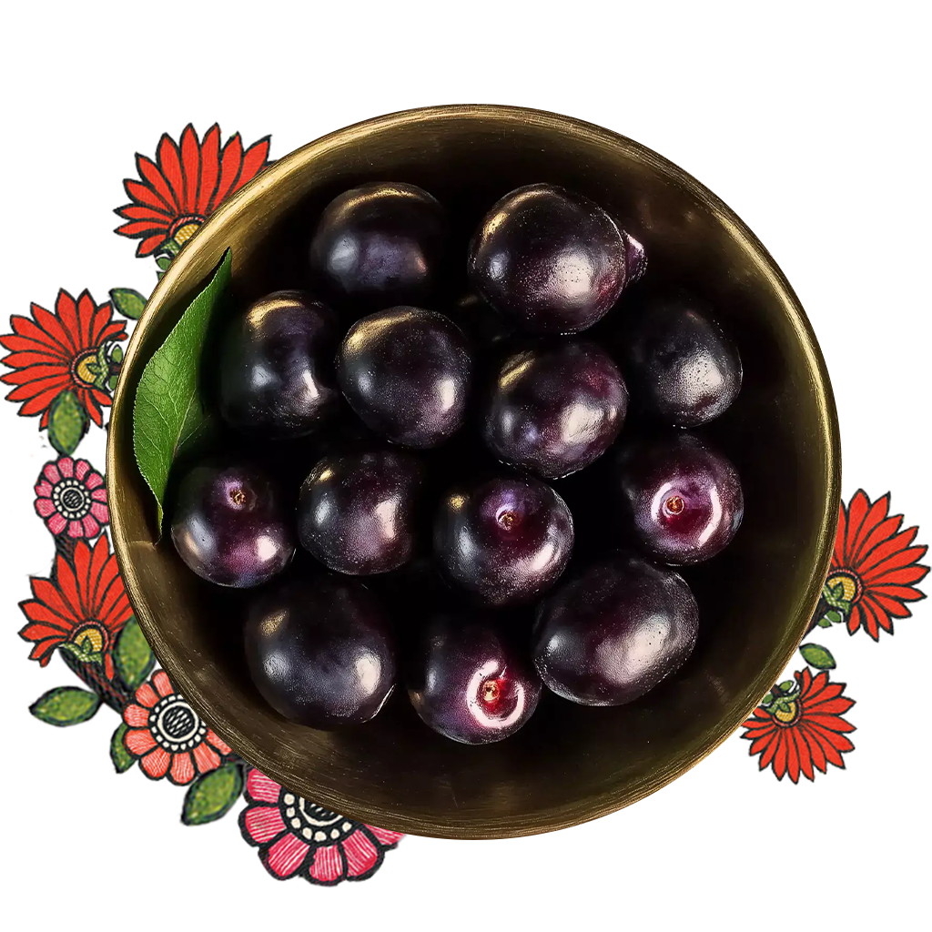 Black plums kept in a brass bowl over an artwork of a pink flower