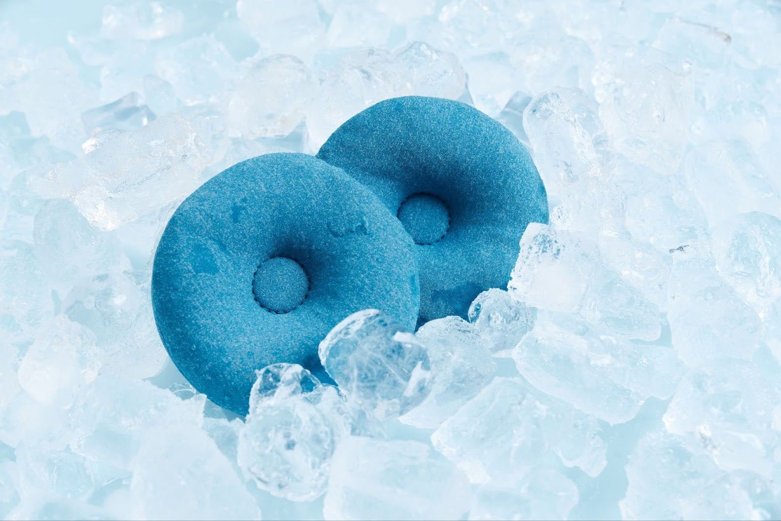 Two circular cooling eye cups sitting on ice cubes.
