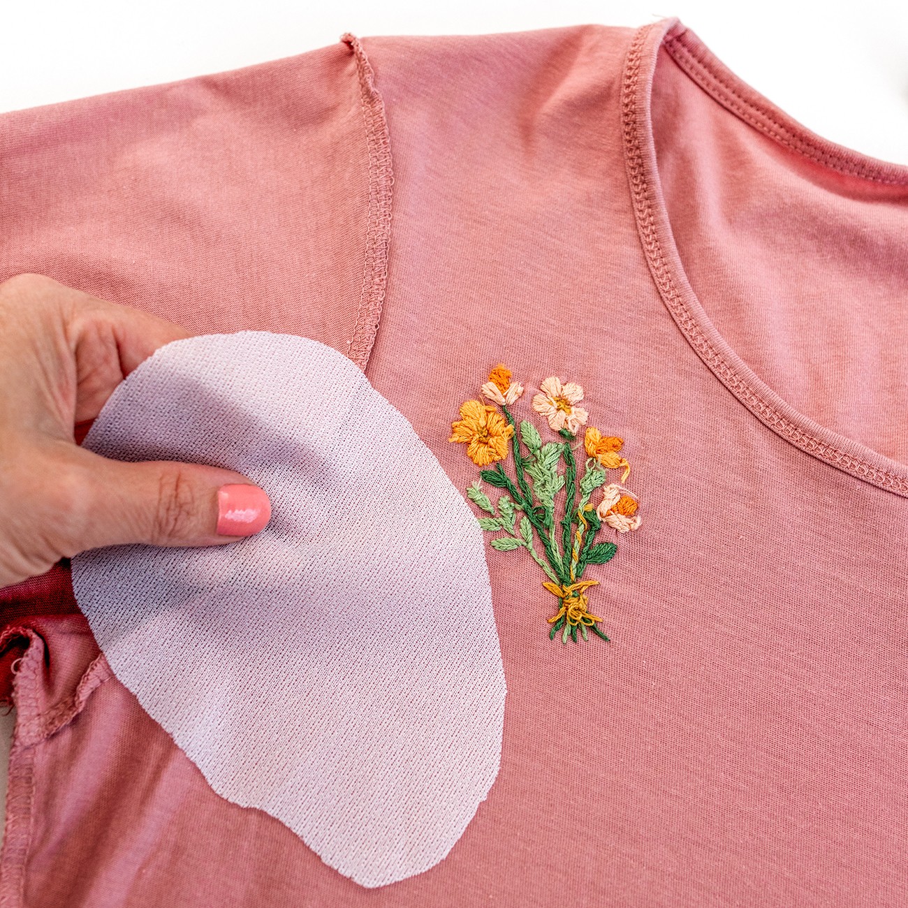 A piece of Cover-a-Stitch is held next to the back of a floral design.