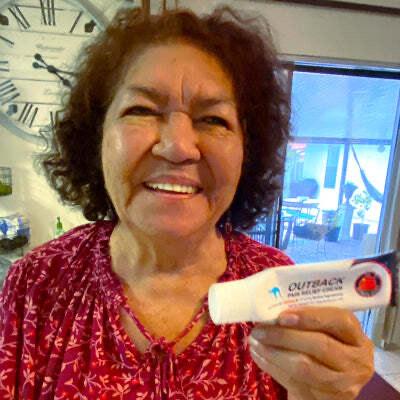 older woman smiling and holding up a used bottle of Outback Pain Cream