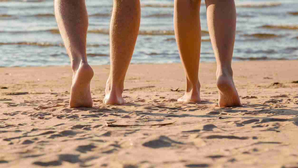 Young couple's barefoot going to swim in cold sunny day. Woman legs have goosebumps. Back view. Closeup