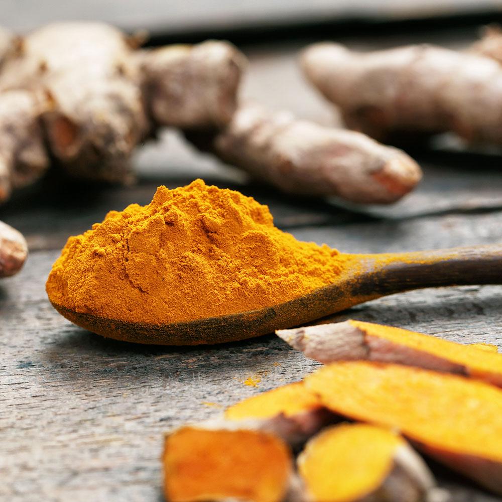 Turmeric powder with wooden spoon and turmeric roots