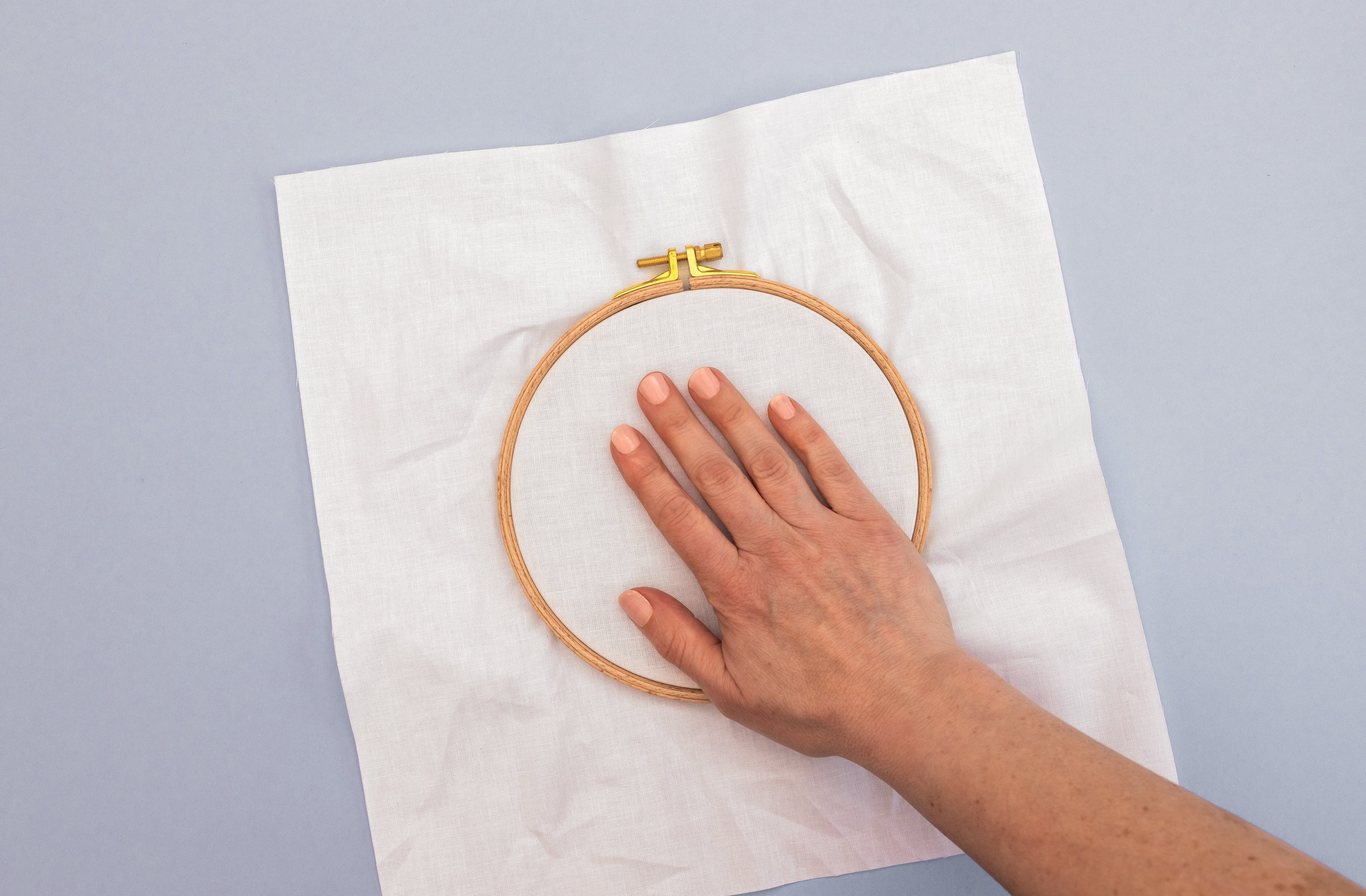 A hand presses down on the fabric in the hoop.