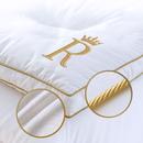 Close-up of white Royal Therapy mattress pad showing gold R embroidery, gold piping, and cotton fabric