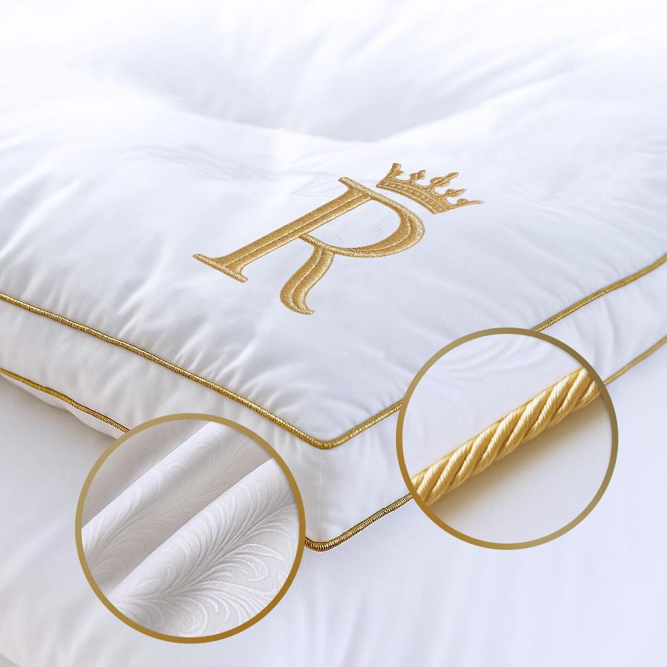 Close-up of white Royal Therapy mattress pad showing gold R embroidery, gold piping, and cotton fabric