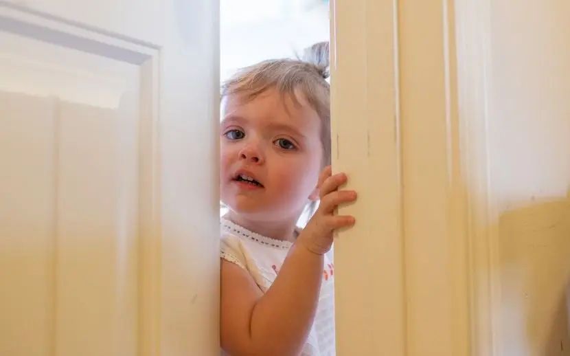 A young child peeks through a slightly open door when childproofing is not present