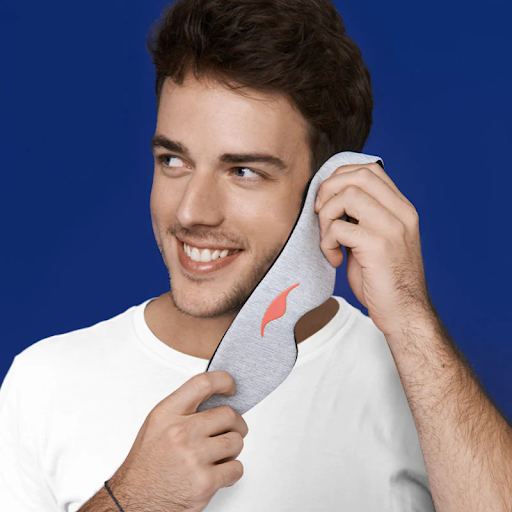 A smiling man holding a Manta Sleep Mask against his face.