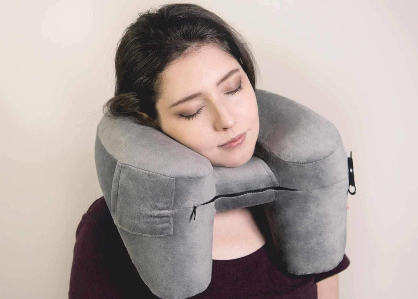 A sleeping woman resting her head on a travel pillow for falling asleep on a long flight.