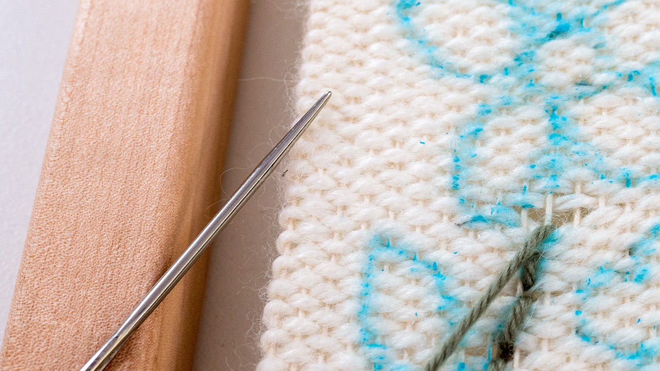 A needle rests on a weaving.