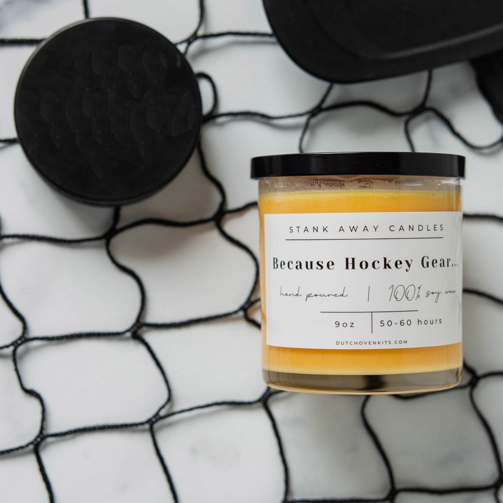 An orange candle sweet orange and chili pepper scent on a hockey net background with hockey pucks. Because hockey gear