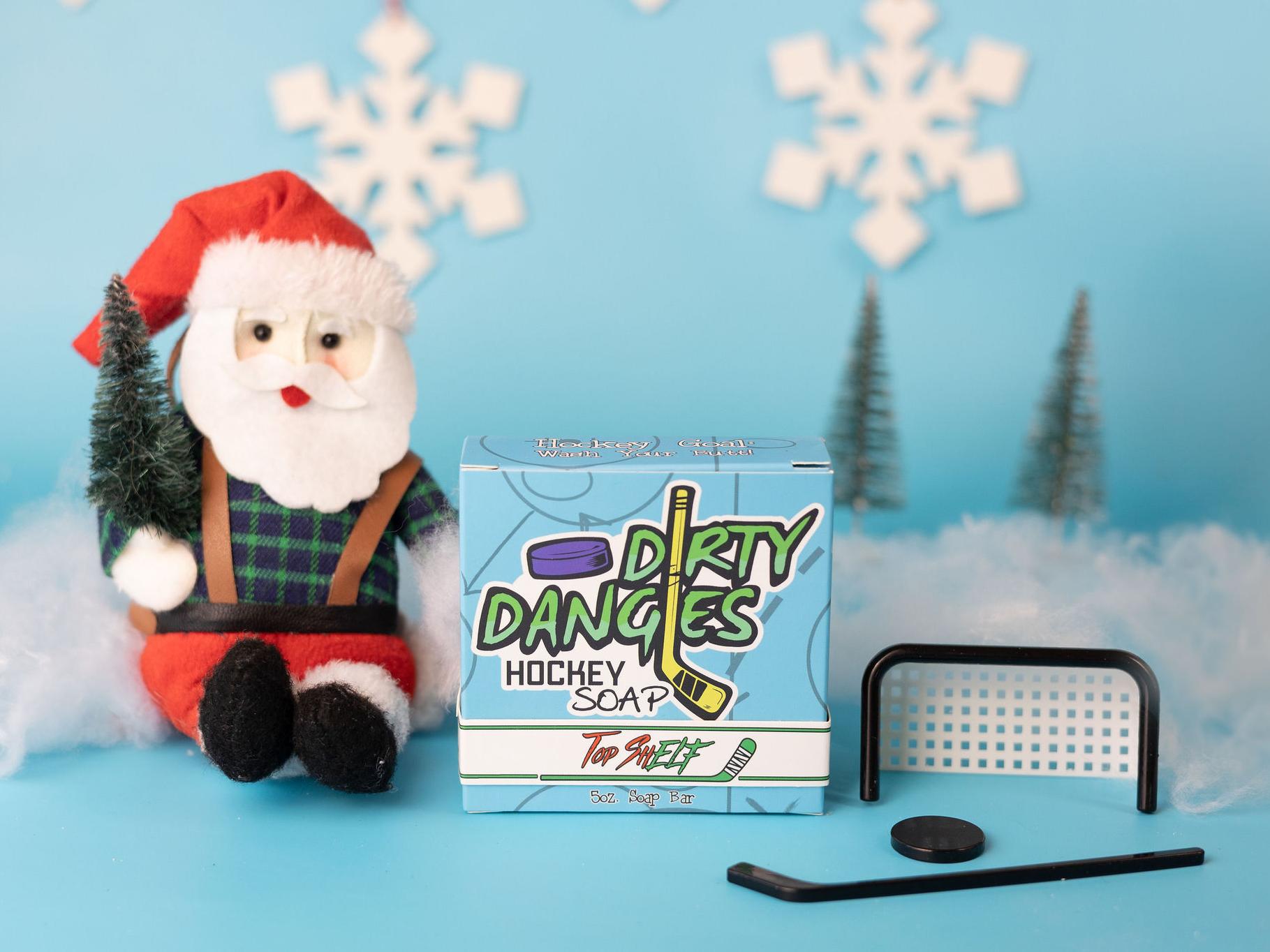 top shelf oatmeal spice christmas hockey soap on a blue Christmas background with a stuffed Santa Claus and a tiny hockey goal, puck and stick.