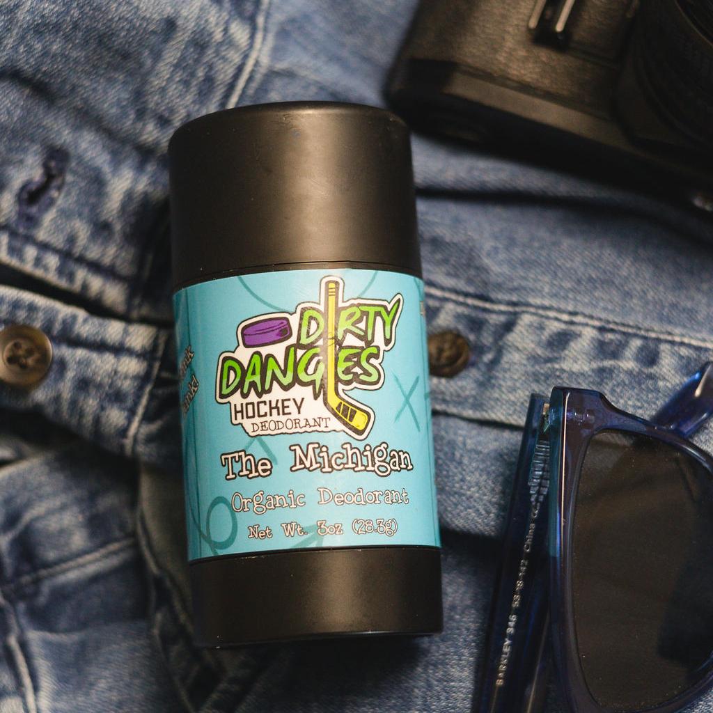 aluminum-free deodorant the michigan scent laying on a pair of jeans with sunglasses and a wallet