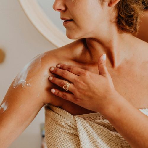 woman applying lotion after shower, still wrapped in towel.